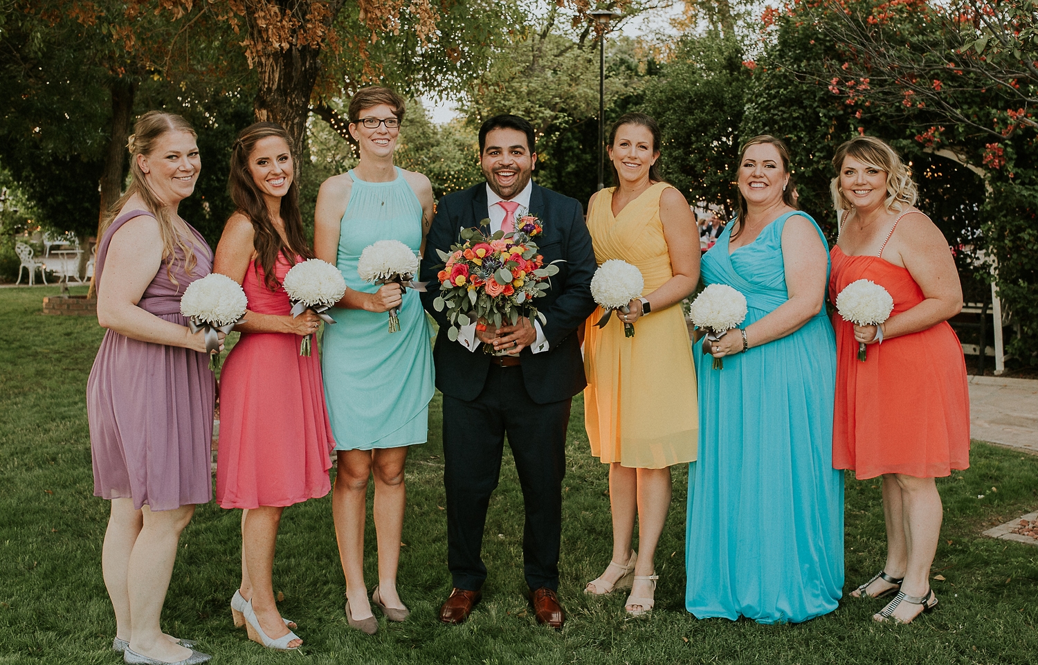 Groom with bridesmaids in bright, mismatched dresses